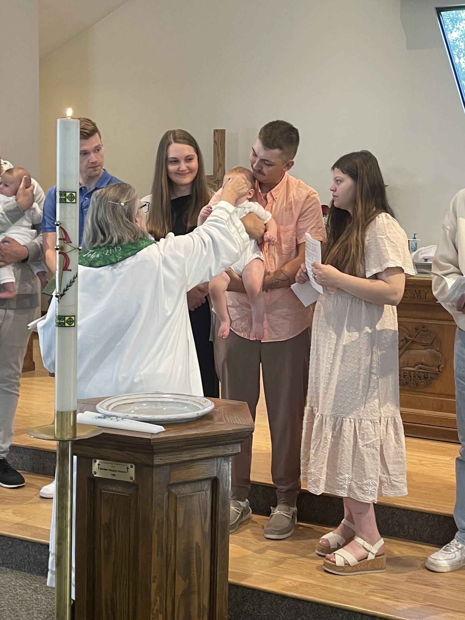person baptizing a baby in a church surrounded by family members